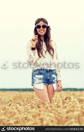 nature, summer, youth culture and people concept - smiling young hippie woman in sunglasses chewing straw on cereal field