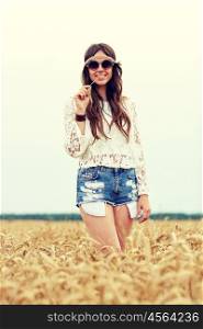 nature, summer, youth culture and people concept - smiling young hippie woman in sunglasses chewing straw on cereal field