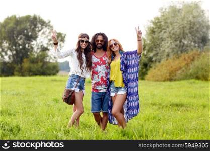 nature, summer, youth culture, gesture and people concept - smiling young hippie friends in sunglasses showing peace hand sign on green field