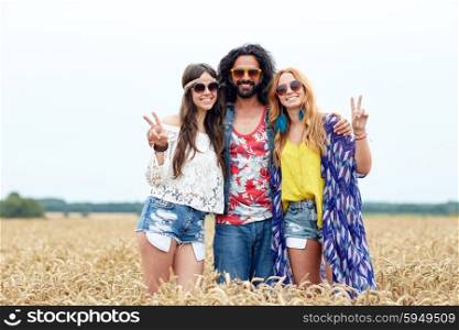 nature, summer, youth culture, gesture and people concept - smiling young hippie friends in sunglasses showing peace hand sign on cereal field