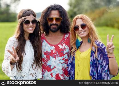 nature, summer, youth culture, gesture and people concept - smiling young hippie friends in sunglasses showing peace hand sign on green field