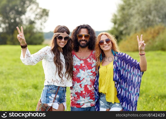 nature, summer, youth culture, gesture and people concept - smiling young hippie friends in sunglasses showing peace hand sign on green field