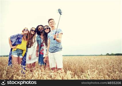 nature, summer, youth culture, technology and people concept - smiling young hippie friends in sunglasses taking picture by smartphone on selfie stick on cereal field