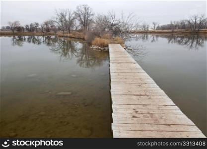 nature trail - boardwalk pathway over lake in old gravel quarry converted into park (Riverbend Ponds in Fort Collins, Colorado), late fall nostalgic scenery