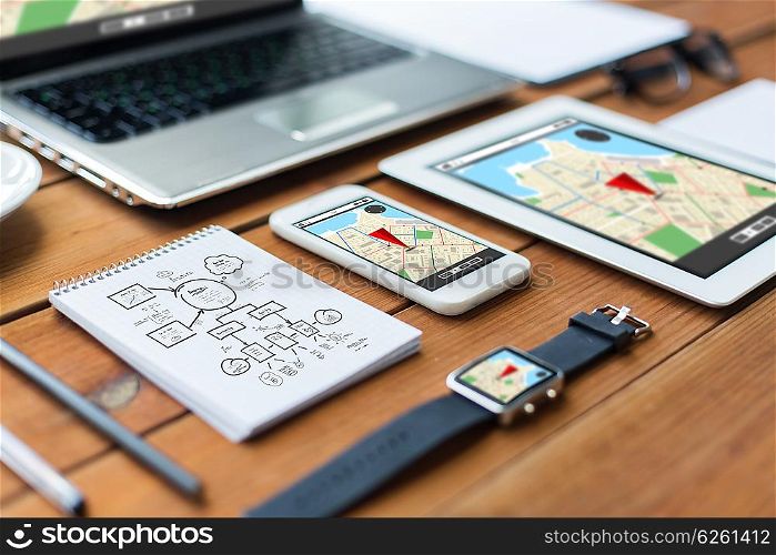 navigation, travel and technology concept - close up of laptop computer, tablet pc, notebook and smartphone with scheme and gps navigator map on wooden table