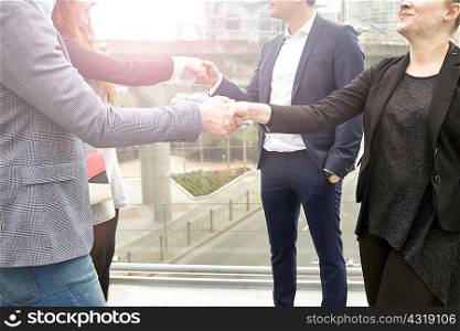 Neck down view businesswomen and men shaking hands on city footbridge, London, UK