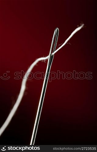 Needle with thread on darkly red background
