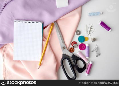 needlework and tailoring concept - scissors, sewing buttons, spools of thread, cloth and notepad with pencil. scissors, sewing tools, cloth and notepad