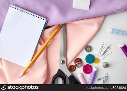 needlework and tailoring concept - scissors, sewing buttons, spools of thread, cloth and notepad with pencil. scissors, sewing tools, cloth and notepad