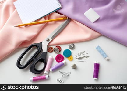 needlework and tailoring concept - scissors, sewing buttons, spools of thread, cloth and notepad with pencil. scissors, sewing tools, cloth and notepad. scissors, sewing tools, cloth and notepad
