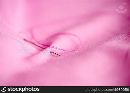 needlework and tailoring concept - sewing needle with thread stuck into pink fabric. sewing needle with thread stuck into pink fabric