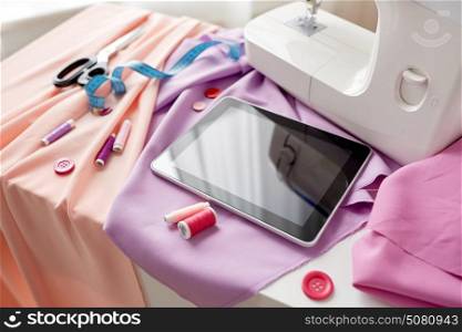 needlework, technology and tailoring concept - sewing machine with tablet pc computer, scissors, tape measure and fabric. sewing machine, tablet pc, scissors and ruler