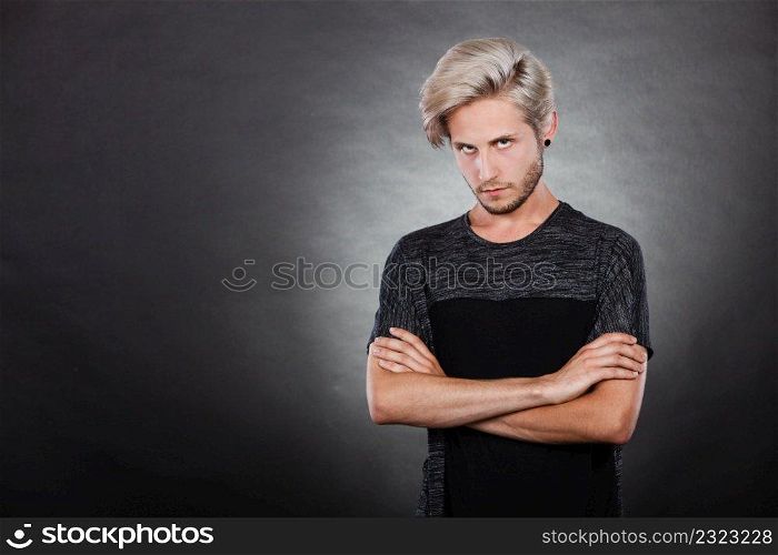 Negative emotion, feelings attitude. Angry grumpy young man looking very displeased standing with arms folded, serious face expression on dark. Angry serious young man, negative emotion