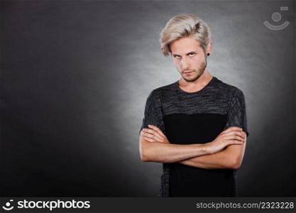 Negative emotion, feelings attitude. Angry grumpy young man looking very displeased standing with arms folded, serious face expression on dark. Angry serious young man, negative emotion
