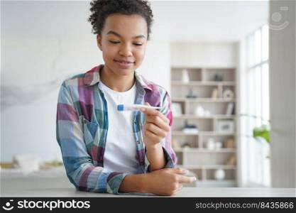 Negative pregnancy stripe test result. Happy african american teenage girl has pregnancy test at home. Hispanic young woman is satisfied and smiling. Baby planning and contraception concept.. Negative pregnancy stripe test result. Young hispanic woman is satisfied and smiling.