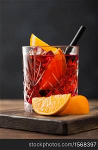 Negroni cocktail in crystal glass with orange slice and black straw on chopping board on wood background. Macro