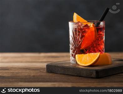 Negroni cocktail in crystal glass with orange slice and black straw on chopping board on wood background. Space for text