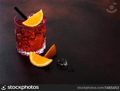 Negroni cocktail in crystal glass with orange slice and black straw on brown table background. Macro