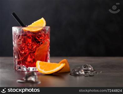 Negroni cocktail in crystal glass with orange slice and black straw on brown table background. Space for text