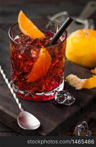 Negroni cocktail in crystal glass with orange slice on chopping board with spoon on wooden background.