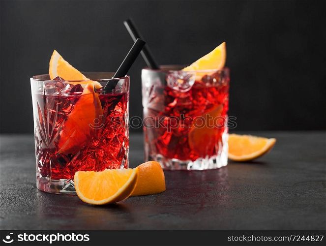Negroni cocktail in crystal glasses with orange slice and black straw on black table background. Macro