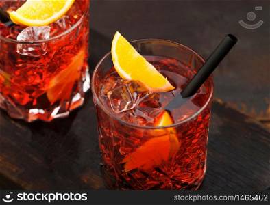 Negroni cocktail in crystal glasses with orange slice and black straw on dark background.