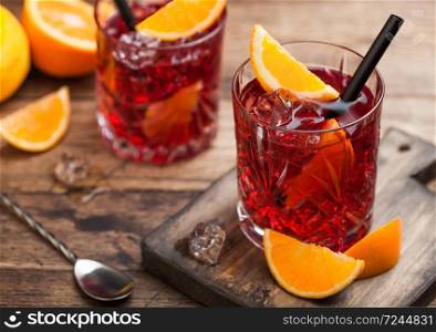 Negroni cocktail in crystal glasses with orange slice and fresh raw oranges on chopping board with strainer on wood background. Top view