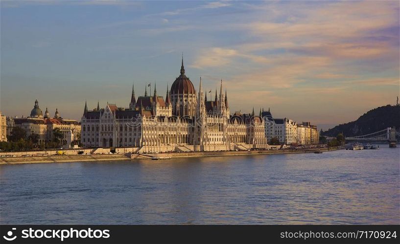 Neo-gothic Hungarian Parliament Building in the Pest side of Budapest and on the banks of River Danube at sunset.