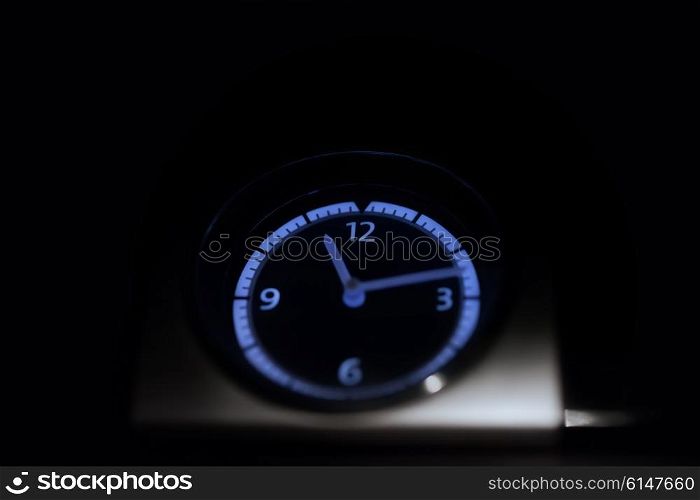 Neon clock on dashboard of car glowing in the dark