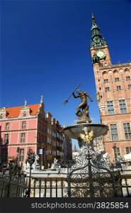 Neptune&apos;s Fountain with blue sky and town hall in the background, Gdansk, Poland. Statue, dating from 1549.