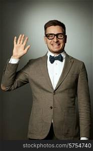 Nerd in eyeglasses and bow tie says Hello against grey background