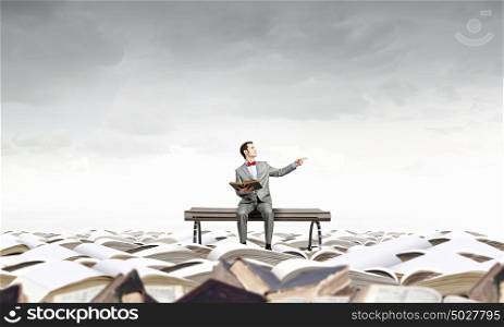 Nerd with book. Young businessman sitting on bench with book in hands and pointing with finger