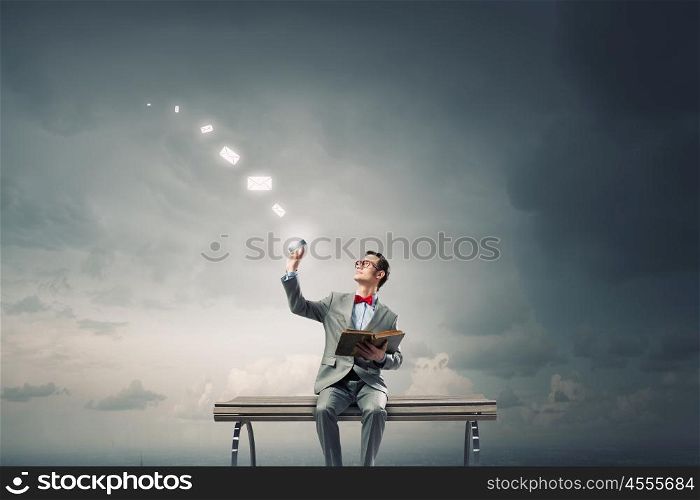 Nerd with book. Young businessman sitting on bench with book in one hand and mobile phone in other