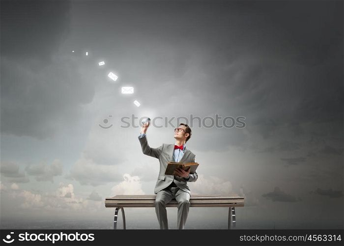 Nerd with book. Young businessman sitting on bench with book in one hand and mobile phone in other