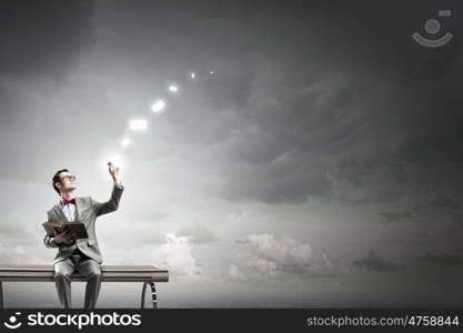 Nerd with book. Young businessman sitting on bench with book in one hand and mobile phone in other