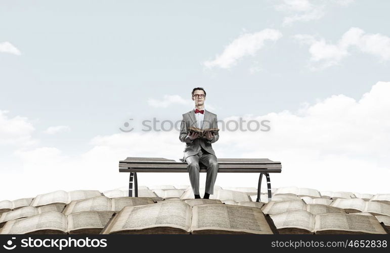 Nerd with book. Young businessman wearing red bow tie sitting on bench with book in hands