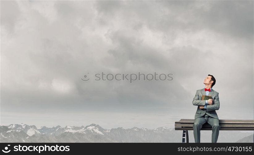 Nerd with book. Young businessman wearing red bow tie sitting on bench with book in hands