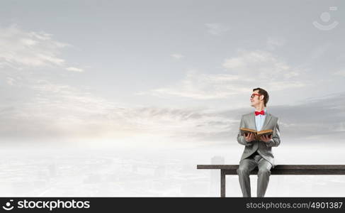 Nerd with book. Young businessman wearing red bow tie sitting on bench with book in hands