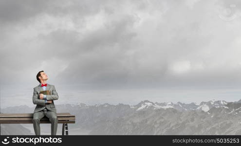 Nerd with book. Young businessman wearing red bow tie sitting on bench with book in hands