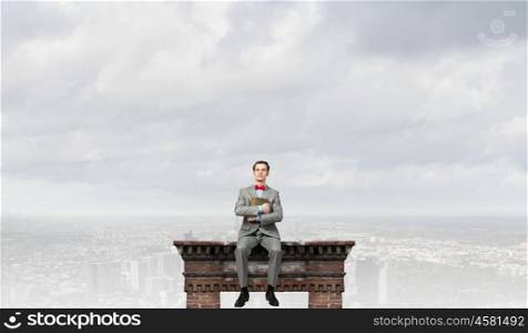 Nerd with book. Young businessman wearing red bow tie sitting on building top with book in hands