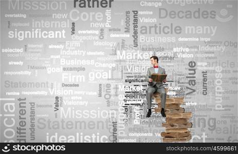 Nerd with book. Young businessman wearing red bow tie sitting on pile of old books