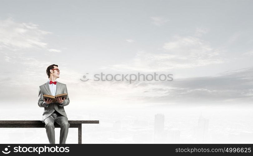 Nerd with book. Young businessman wearing red bow tie sitting with book in hands