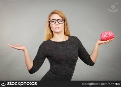 Nerdy woman in big eyeglasses having confused face expression pointing with palm open hand and holding brain. Woman in eyeglasses being confused holding brain