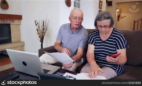 Nervous senior couple calculating the bills at home with laptop computer. Pensioners being frustrated by the costs of their bills. Handheld movement