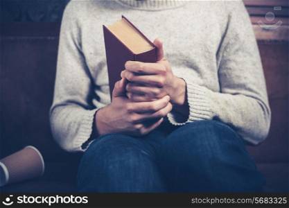 Nervous young man is clutching a book and spilling coffee on the sofa
