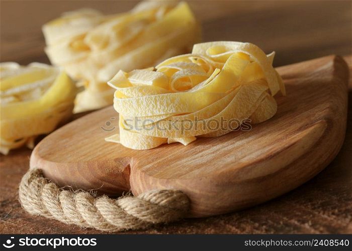 Nest of pasta tagliatelle on wooden cutting board aon rustic background. Selective focus