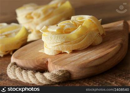 Nest of pasta tagliatelle on wooden cutting board aon rustic background. Selective focus