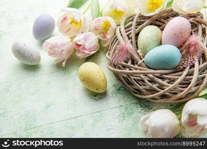 Nest with Easter eggs painted pastel colors and pink tulips on a green wooden background. Top view. Space for text.