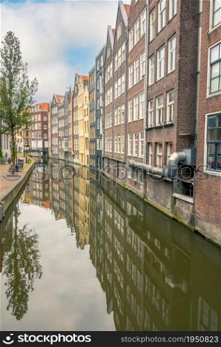 Netherlands. Amsterdam canal with industrial buildings. Reflections of houses and trees. Bicycles on the waterfront. Houses on the Canal of Amsterdam in an Industrial Area