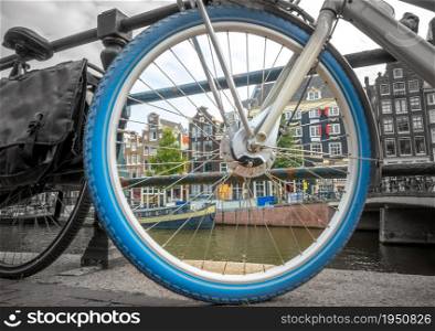 Netherlands. Bicycle wheel on the Amsterdam waterfront close-up. Black and white photo of the outside of the wheel rim, color photo inside. Amsterdam Canal Houses in a Bicycle Wheel